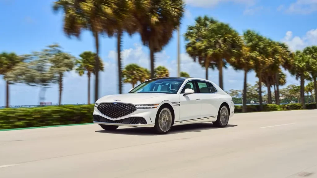 نمای دینامیک از نمای جلویی یک جنسیس G90 سفید مدل ۲۰۲۴ که در بزرگراهی با درختان نخل در پس‌زمینه در حال حرکت است.
جنسیس