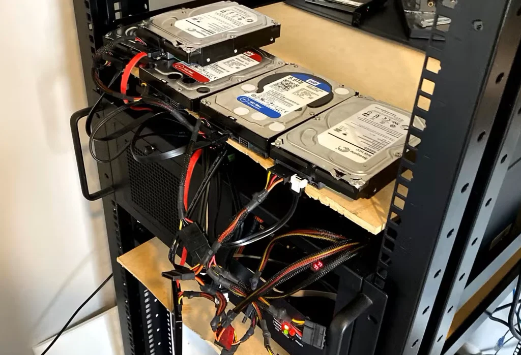 هارد دیسک‌ها روی قفسه قرار دارند و کابل‌ها از همه جا به یک کامپیوتر نصب شده در رک متصل هستند.
